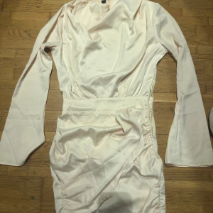 Vit  omlottklänning från Bik Bok - Elegant kräm vit omlottklänning från Bik Bok i satin. Klänningen har långa ärmar och en smickrande omlottdesign som ger en fin siluett. Perfekt för speciella tillfällen.