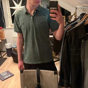 Grön pikétröja från Ralph Lauren - Säljer en klassisk grön pikétröja från Ralph Lauren med broderad logotyp på bröstet. Tröjan har korta ärmar och knappar vid kragen. Perfekt för en stilren look.