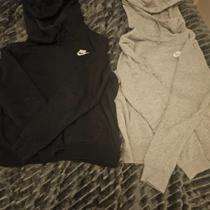 Svart och grå hoodie från Nike - Två klassiska hoodies från Nike i svart och grått. Båda har en justerbar huva med dragsko och den ikoniska Nike-loggan på bröstet. Perfekta för en avslappnad stil.