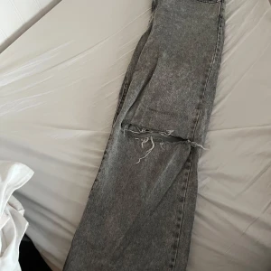 Grå jeans med slitna detaljer - Säljer ett par grå jeans från Denim med coola slitna detaljer vid knäna. Perfekta för en avslappnad look. De har en klassisk design med fem fickor och knappgylf.