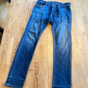 Blå jeans från Diesel med slitningar - Snygga blå jeans från Diesel med en klassisk straight passform. De har en knappgylf och femficksdesign. Perfekta för en avslappnad stil.