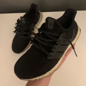 Svarta Adidas Ultraboost - Säljer ett par svarta Adidas Ultraboost med stickad ovandel och snörning. Skorna har en bekväm och responsiv sula, perfekt för löpning eller vardagsbruk.