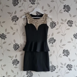 Svart klänning med paljettdetaljer, Strl: 36/S eu size,  - Elegant svart klänning med glittrande paljetter på axlarna och en volangdetalj i midjan. Klänningen är ärmlös och har en figurnära passform som ger en stilren siluett.
