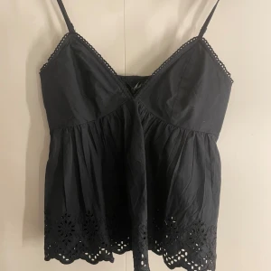 Svart bikbok top - Snygg svart ärmlös topp med smala axelband och vackra spetsdetaljer längs kanterna. Toppen har en luftig passform och dekorativa broderier längst ner. Toppen är endast provad med prislapp kvar och som ny.