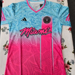 Fotbollströja från Adidas - Snygg fotbollströja från Adidas i en cool turkos och rosa färgkombination. Tröjan har ett unikt mönster med palmer och vågor, samt korta ärmar. Perfekt för att sticka ut på planen!