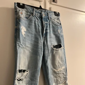 Ljusa jeans med hål - Säljer ett par mid waist, ljusa jeans med slitningar och hål för en trendig look. Jeansen har en rak passform och är tillverkade i denim. Bra men använt skick🩵