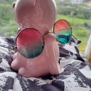 Runda solglasögon med färgskiftande glas - Snygga runda solglasögon med färgskiftande glas i rosa och grönt. Glasögonen har en tunn guldfärgad metallram som ger en retro känsla. Perfekta för att ge din stil en unik touch. Har små repor i glaser, men det syns inte när du bär dem.