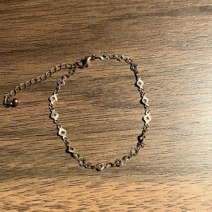 Guldfärgat armband med justerbar kedja - Elegant guldfärgat armband med små blommönster och en justerbar kedja för perfekt passform. Perfekt för att lägga till en subtil glans till din outfit.