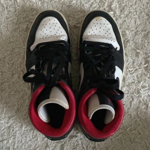 Nike Air Jordans i svart, vitt och rött - Snygga Nike Air Jordans i klassisk färgkombination av svart, vitt och rött. Skorna har snörning och den ikoniska Air Jordan-loggan på sidan. Perfekta för dig som vill ha en stilren och sportig look. Kommer med en skobox.