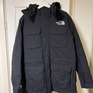 Svart jacka från The North Face - Säljer en svart jacka från The North Face med huva och flera praktiska fickor. Jackan har en dragkedja framtill och är perfekt för kyligare väder. Den är långärmad och har en stilren design med logotyp på bröstet och ryggen.