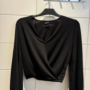 Svart omlottopp från Gina Tricot - Snygg svart omlottopp från Gina Tricot med långärmad design och v-ringad hals. Perfekt för en stilren look.