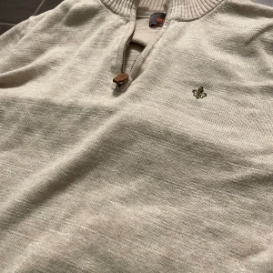 Morris tröja - Snygg beige tröja med ribbad krage och knappdetalj. Broderad logga på bröstet ger en stilren touch. Perfekt för en avslappnad look.