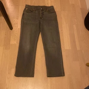 Grå jeans från Levi's - Säljer ett par grå jeans från Levi's med klassisk femficksdesign och knappgylf. Byxorna har en rak passform och är perfekta för en avslappnad stil. Levi's-loggan syns på bakfickan. Storlek 14a passar dig som är 160-170, aldrig använda