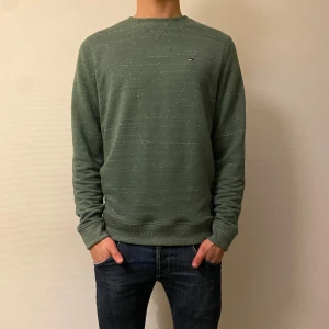 Grön tröja från Tommy Hilfiger - Säljer en stilren grön tröja från Tommy Hilfiger med diskret logga på bröstet. Storlek L men passar mer som M. Tröjan har långa ärmar och en normal passform, perfekt för en avslappnad look. Passar bra till jeans eller chinos.