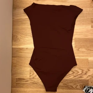 Brun bodysuit - Snygg brun bodysuit med korta ärmar och en elegant design. Perfekt för att matcha med jeans eller kjol för en stilren look.