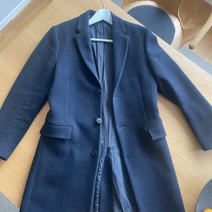 Marinblå ullblandad rock från MNG Man - Elegant marinblå rock från MNG Man i ullblandning. Rocken har en klassisk design med knappar framtill och långa ärmar. Perfekt för kyligare dagar med sin stilrena look.