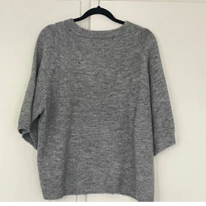 Grå stickad tröja - Mysig grå stickad tröja med trekvartsärm. Perfekt för kyligare dagar och enkel att matcha med jeans eller kjol.