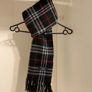 Burberry  - Säljer nu denna snygga halsduk från Burberry i svart, Tillverkad i 100% kashmir med klassiskt mönster och fransar i ändarna. Den är i micket fint skick utan några defekter alls. Perfekt för att hålla dig varm och stilren under kyliga dagar. Hör av er vid minsta funderingar☺️