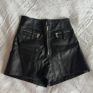 Svarta skinnshorts från Tiger Mist - Svarta högmidjade läder shorts från Tiger Mist med dragkedja. Strl small