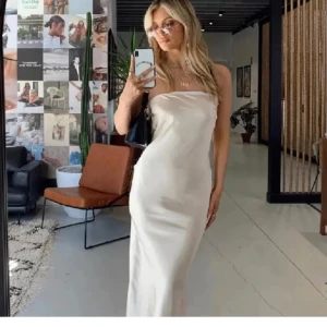 Vit axelbandslös balklänning - Elegant vit axelbandslös klänning i satin med en stilren design. Klänningen har en vacker knytning i ryggen och en lång siluett som ger en sofistikerad look. Perfekt för speciella tillfällen. Klänningen är i nyskick därmed aldrig använd, prislapp finns kvar på!☺️