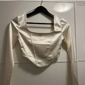Vit satin korsett från H&M - Säljer en superfin vit korsett från H&M i satinmaterial. Den har en elegant och stilren design med långa ärmar och en tight passform. Perfekt för festliga tillfällen eller när du vill känna dig extra glamorös. Ny och oanvänd med prislapp kvar!