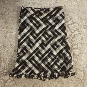Vintage rutig kjol - Säljer en superfin svartvit rutig kjol från Cherry i storlek 38. Kjolen har ett klassiskt rutmönster och är dekorerad med fransar längst ner. Perfekt för höst och vinter. Vintage midi kjol