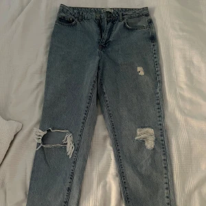 Blå jeans med slitningar - Säljer ett par snygga blå jeans från Ginatricot i storlek 38. De har coola slitningar på benen som ger en avslappnad och trendig look. 