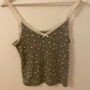 Coquette topp  - Jätte söt topp med rosa blommor och spets<33 basfärgen är en mörkare grön och blommorna är ljusrosa💕 man kan tyvärr inte ändra band- längden men man kan enkelt sy om den till sin designerade längd:)) 