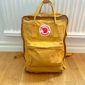 Fjällräven kånken ryggsäck - Fin gul ryggsäck som ej kommer till användning 💛 Köpt för ca 5 år sedan på naturkompaniet. Skicket är helt ok, men den har lite fläckar på vissa ställen och är smutsig i botten. Den går att tvätta! Den har två fack för vattenflaskor och sittunderlag☺️