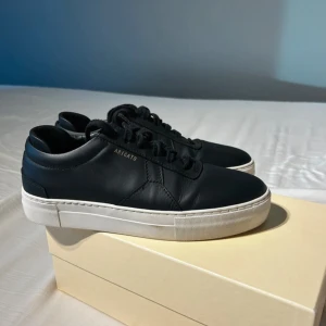 Svarta sneakers från Axel Arigato - Säljer ett par stilrena svarta sneakers från Axel Arigato. De är gjorda i skinn och har en vit sula som ger en snygg kontrast. Perfekta för både vardag och fest! Som är använda ett par gånger men är fortfarande väldigt fräscha 