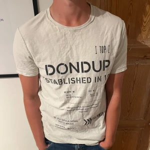 Vit t-shirt från Dondup - Säljer en snygg vit t-shirt från Dondup med tryck på framsidan. Den är kortärmad och perfekt för en avslappnad stil. . Sitter som en liten medium. Finns dock två små hål i nacken!