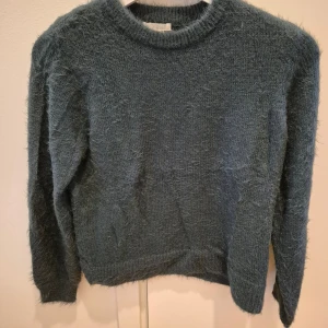 Stickad tröja HM - Stickad tröja från HM. Mjuk, lurvig, gosig och sticks inte! Kan ha den utanför eller innanför byxorna. Mörkgrön färg. Använd fåtal gånger. Hårar inte! Storlek XS. 60% polyamid, 30% akryl. Axelbredd 35 cm, längd 58 cm.