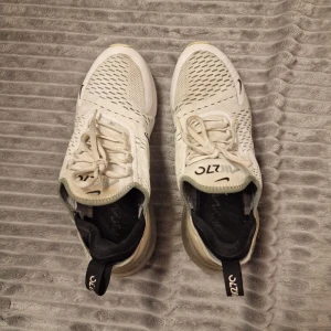 Vita Nike Air Max sneakers - Säljer ett par vita Nike Air Max sneakers med svart detaljering och synlig luftdämpning i sulan. Skorna har snörning och en modern design som passar perfekt för en sportig look.