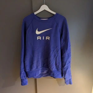 Blå sweatshirt från Nike - Säljer en blå sweatshirt från Nike med det klassiska Nike Air-logotypen i vitt på framsidan. Tröjan har långa ärmar och en rund halsringning. Perfekt för en sportig look eller avslappnade dagar.