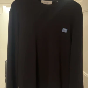 Svart tröja från Les Deux - Säljer en stilren svart tröja från Les Deux med en liten blå detalj på bröstet. Perfekt för en stilren look. 