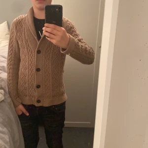 Beige stickad kofta med knappar - Säljer en snygg beige stickad kofta med ett klassiskt flätmönster. Koftan har långa ärmar och stora knappar framtill. Perfekt för kyliga dagar! Ny pris 1299kr mitt pris är 450kr. Mvh Damian