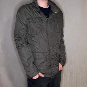 Field Jacka storlek L  - Fieldjacka från East West 🖤🧥 Storlek: L Färg: Mörkgrå ☁️ Ett måste för en klassisk garderob! Modellen på bilden är 183 cm och väger 75 kg.