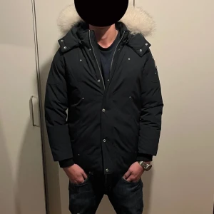 Moose knuckles jacka - Säljer en stilren svart parkajacka från Moose Knuckles med en fluffig pälsdetalj på huvan. Jackan har långa ärmar och knappar framtill. Perfekt för kyliga dagar. Pris ej hugget i sten 🪨 