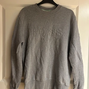 Grå sweatshirt från Hugo Boss - Säljer en stilren grå sweatshirt från Hugo Boss med broderad logga på framsidan. Det är en äldre model som inte säljs längre, och har ett jätte fint skick och har inte använts många gånger, vid frågor eller intresse är det bara skriva
