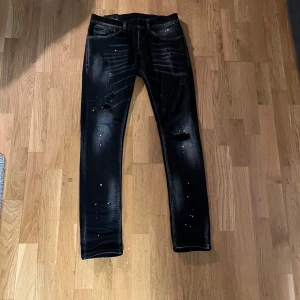 Svarta dondup jeans med slitningar - Snygga svarta dondups med riktigt feta  slitningar. De har en slim passform och är perfekta för en trendig look. Jeansen har klassisk femficksdesign och knappgylf.