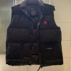 Svart Canada Goose dunväst  - Säljer en svart dunväst från Canada Goose. De är en lite äldre variant med gammal logotyp. Obs (västen är liten i storleken så den passar large men de står XXL)