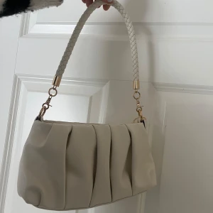 Vit axelväska med flätat handtag - Snygg vit axelväska med ett flätat handtag och dragkedja. Väskan har en stilren design med veckade detaljer på framsidan och backsida. Perfekt till vardag!✨💖💗💗