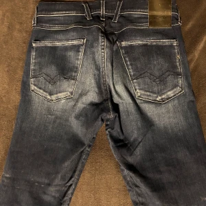 Mörkblå jeans från Replay - Snygga mörkblå jeans från Replay med klassisk femficksdesign och diskreta slitningar. Jeansen har en knappgylf och är tillverkade i ett slitstarkt denimtyg. Perfekta för en avslappnad stil. W31 L32