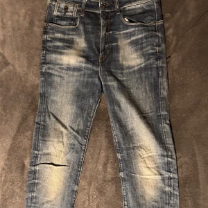 Blå jeans från G-Star RAW - Snygga blå jeans från G-Star RAW med slitna detaljer och klassisk femficksdesign. Jeansen har en knappgylf och är tillverkade i ett robust denimtyg. Perfekta för en avslappnad stil. Storlek W30 L 32