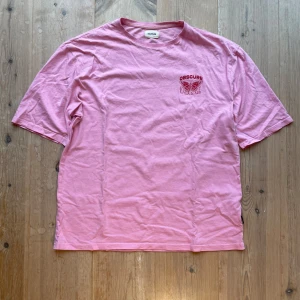 Rosa t-shirt från Yourturn - Säljer en rosa t-shirt från Yourturn med tryck av texten 'OBSCURE FUTURE' och en fjäril i rött. T-shirten har korta ärmar och är tillverkad i bomull. Sitter rätt baggy. Skriv vid frågor!