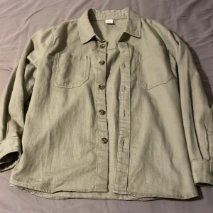 Grön overshirt med knappar - Snygg grön overshirt med knappar framtill och två bröstfickor. Perfekt för lager-på-lager-stil. Den har långa ärmar och en klassisk krage. Passar bra till både jeans och chinos, är dock för små barn. 146-152