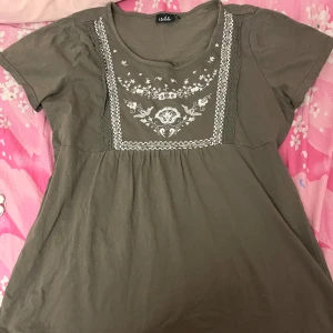 Tröja med broderi - Säljer en olivgrön blus från isolde med vackert vitt broderi framtill. Blusen har korta ärmar. 