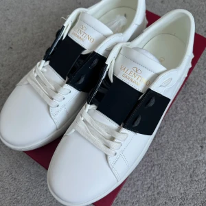 Valentino Garavani vita sneakers - Snygga vita sneakers från Valentino Garavani med svart detalj över snörningen. Skorna har en stilren design med klassisk snörning och en bekväm sula. Perfekta för en trendig look.