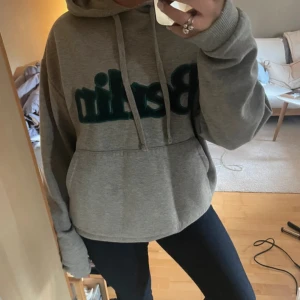 Grå hoodie med text - Säljer en grå hoodie med stor text på framsidan. Den har en bekväm passform med långa ärmar och en klassisk huva. Perfekt för en avslappnad stil.
