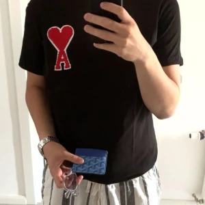 Svart t-shirt från Ami Alexandre Mattiussi - Snygg svart t-shirt från Ami Alexandre Mattiussi med ett rött hjärta och bokstaven 'A' broderat på bröstet. Perfekt för en stilren look. T-shirten är kortärmad och har en normal passform. Sitter som L